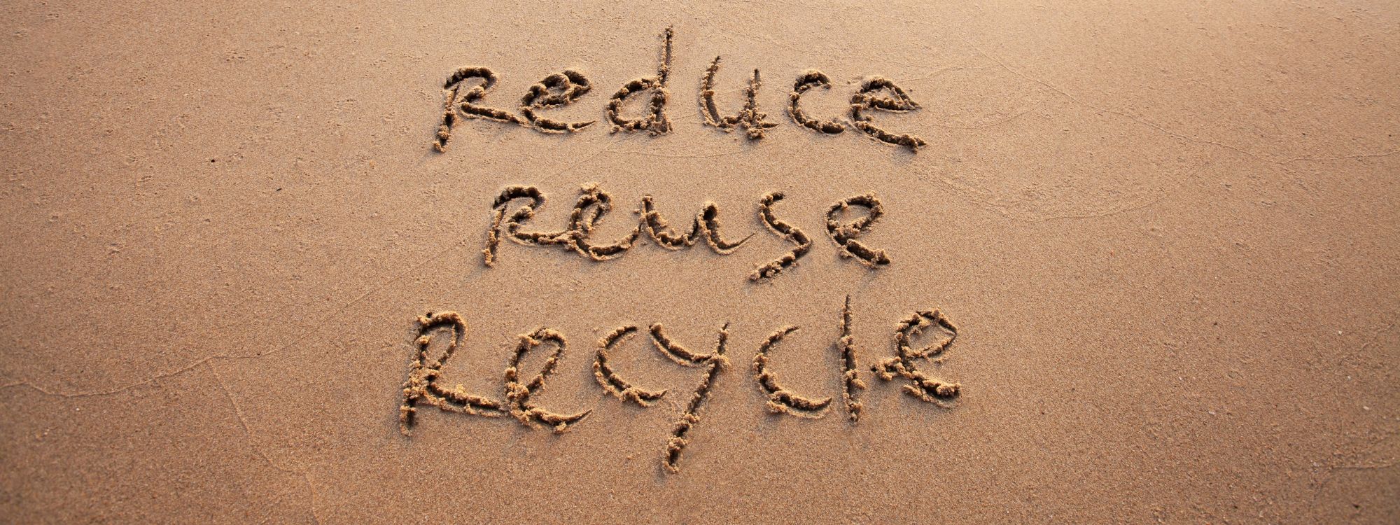 The words Reduce, Reuse, and Recycle drawn in the sand