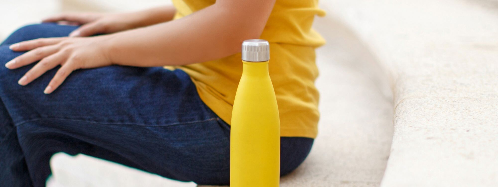 yellow stainless steel water bottle sitting beside seated woman in same color t-shirt